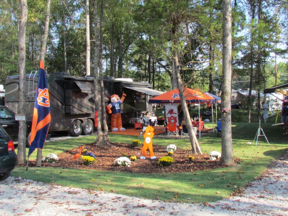 An Auburn-decorated RV site under the pines at University Station, with flags, an awning and a tailgate tent